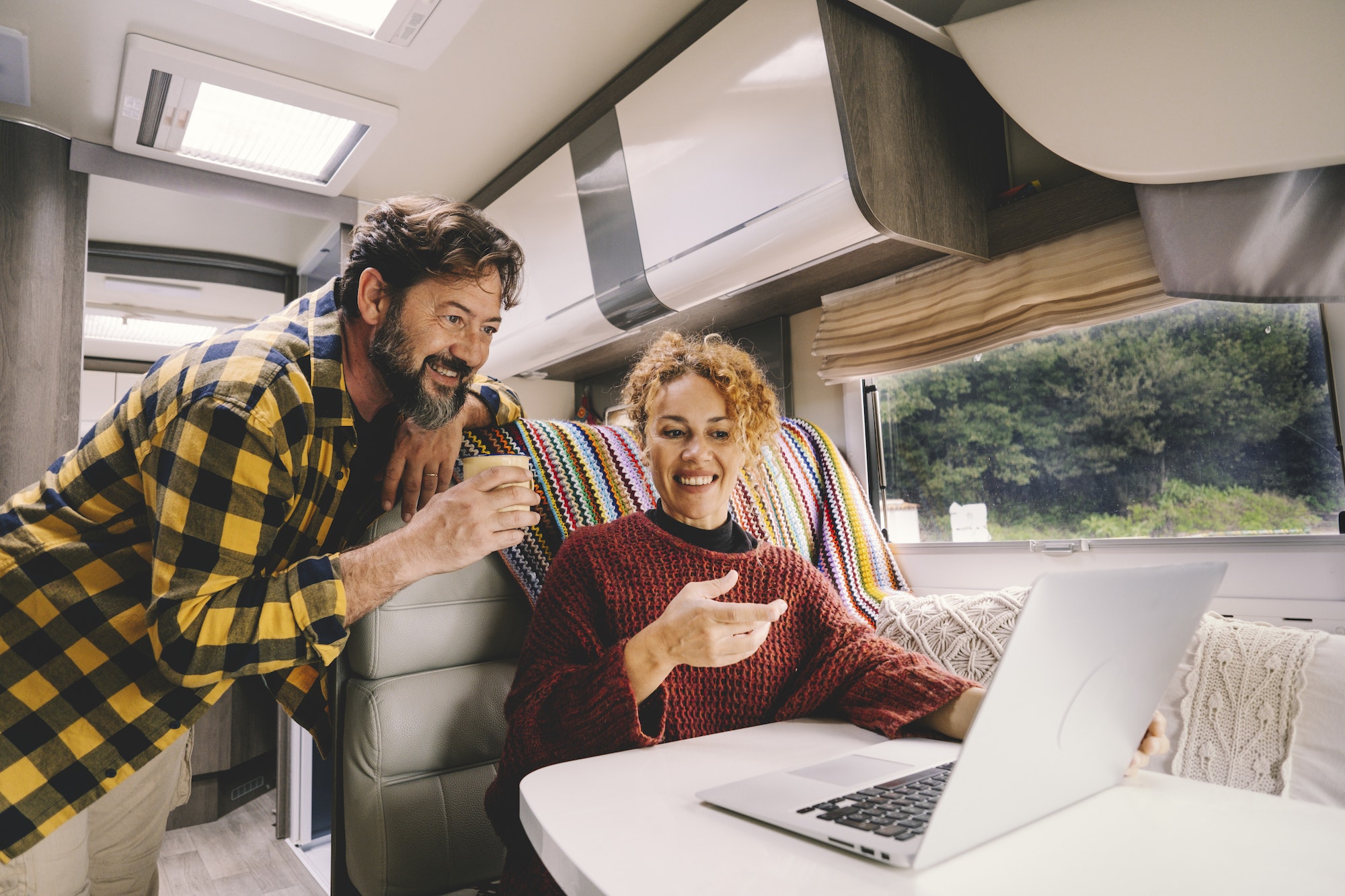 Adult couple enjoy work together using laptop computer sitting inside camper rv vehicle.